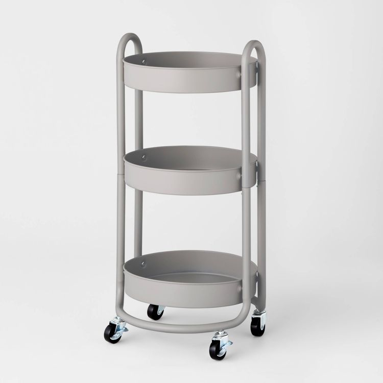 A gray colored utility storage cart with three round shelves and four wheels.