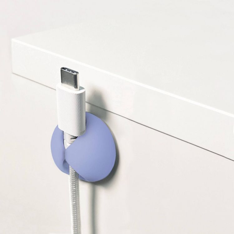 A white USB-C cable is held in place by a light purple colored cable clip attached to the edge of a white surface.