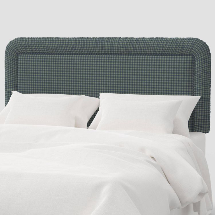 A checkered dark green and blue colored headboard behind a bed with white pillows and sheets.