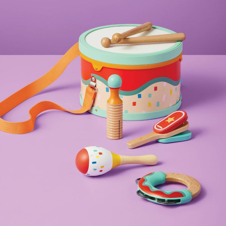 A colorful toy drum set with drumsticks, maracas, a tambourine, and other percussion instruments on a purple surface.