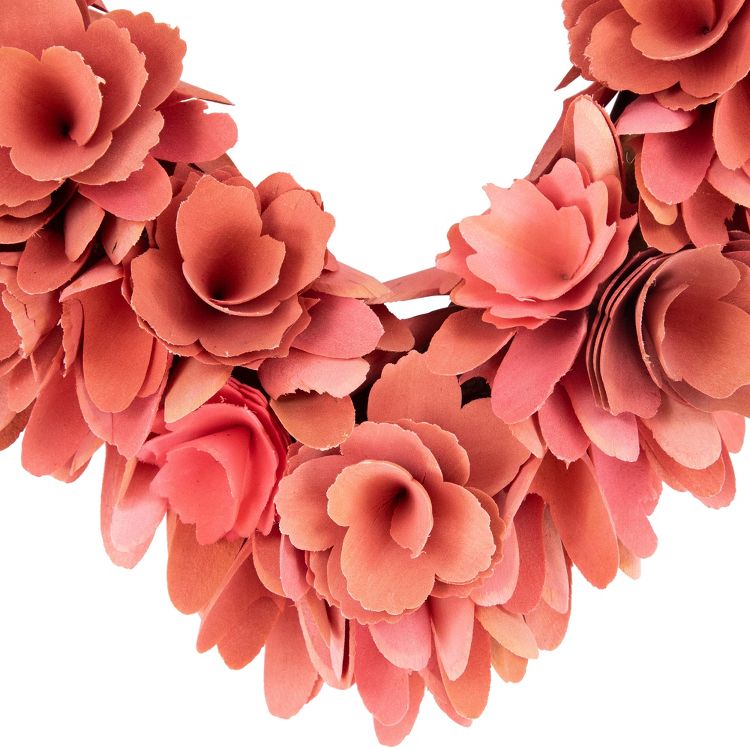 A wreath made of layered, coral colored paper flowers arranged in a circular pattern.