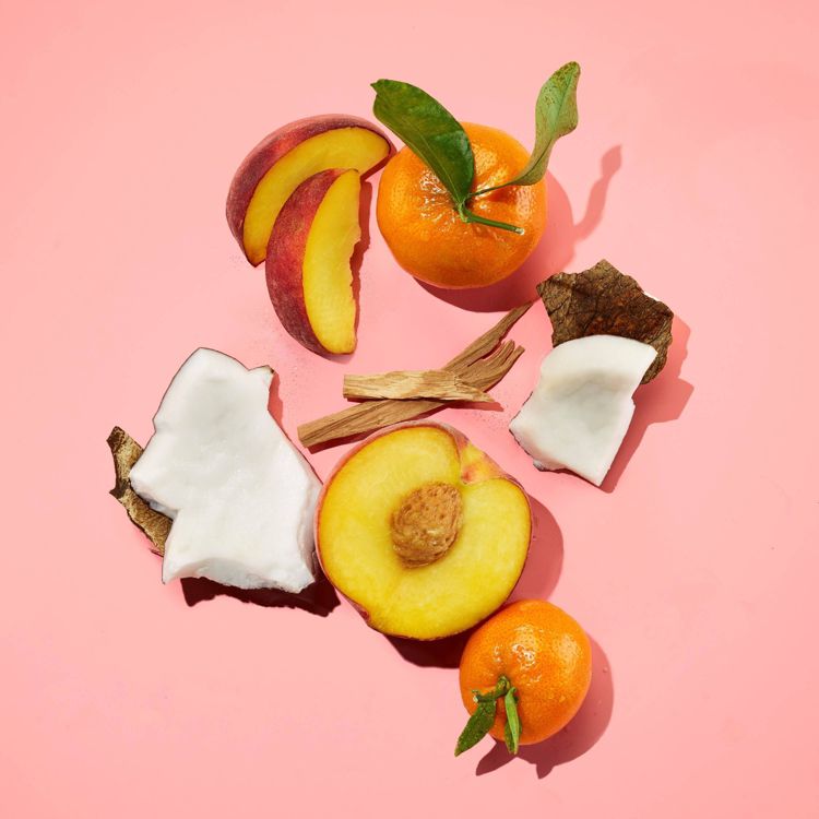 Slices of peach, coconut pieces, whole tangerines, and wood chips arranged on a pink colored background.