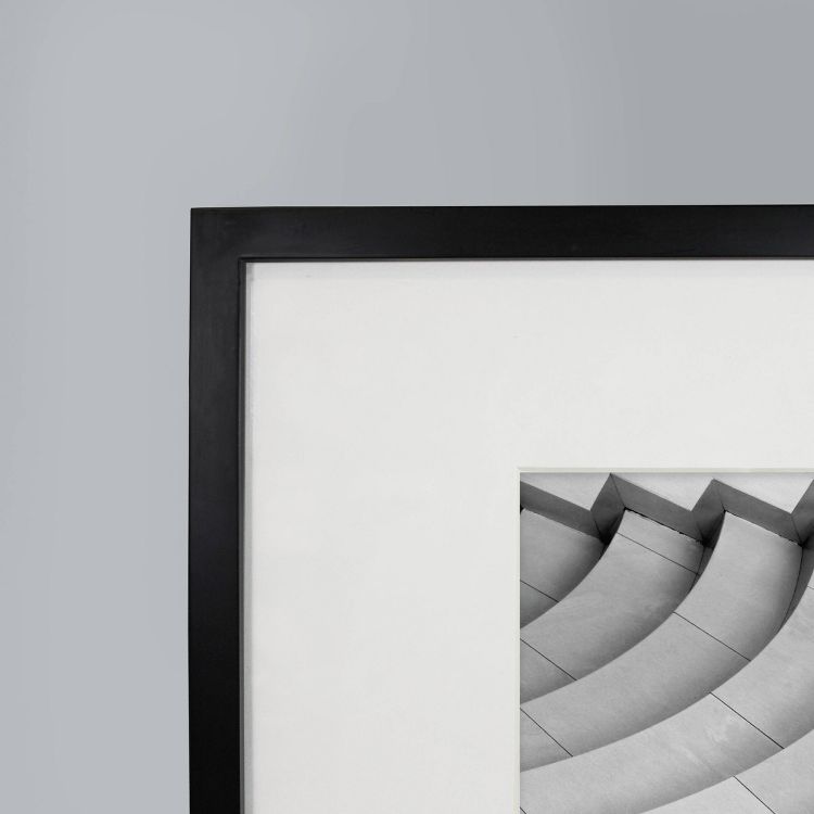A black colored frame with a white mat board displaying a grayscale image of curved steps.