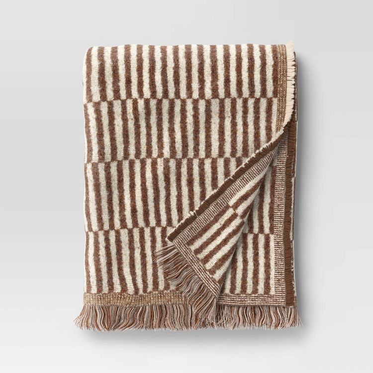A brown and cream colored striped blanket with fringed edges folded neatly.