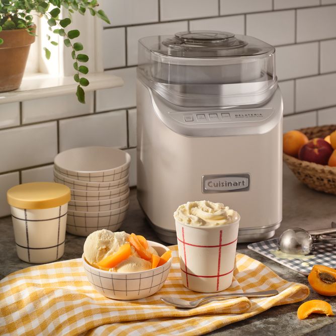 Ice cream maker on countertop. Ice cream bowls with vanilla ice cream topped with peaches.