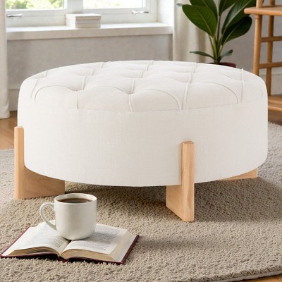 White round tufted ottoman with wooden legs near window