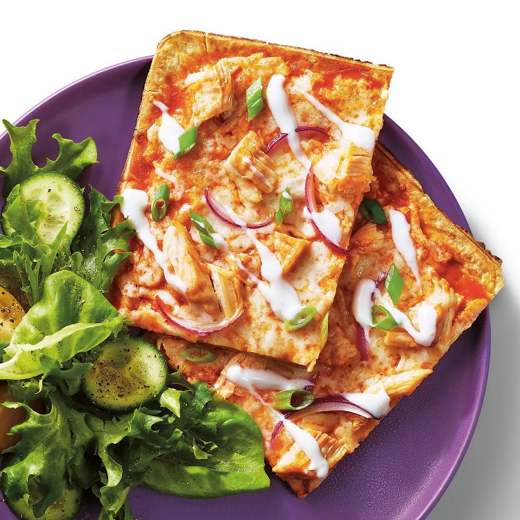Two slices of flatbread pizza topped with chicken, red onion, green onions, and white sauce on a purple plate with a side of salad.