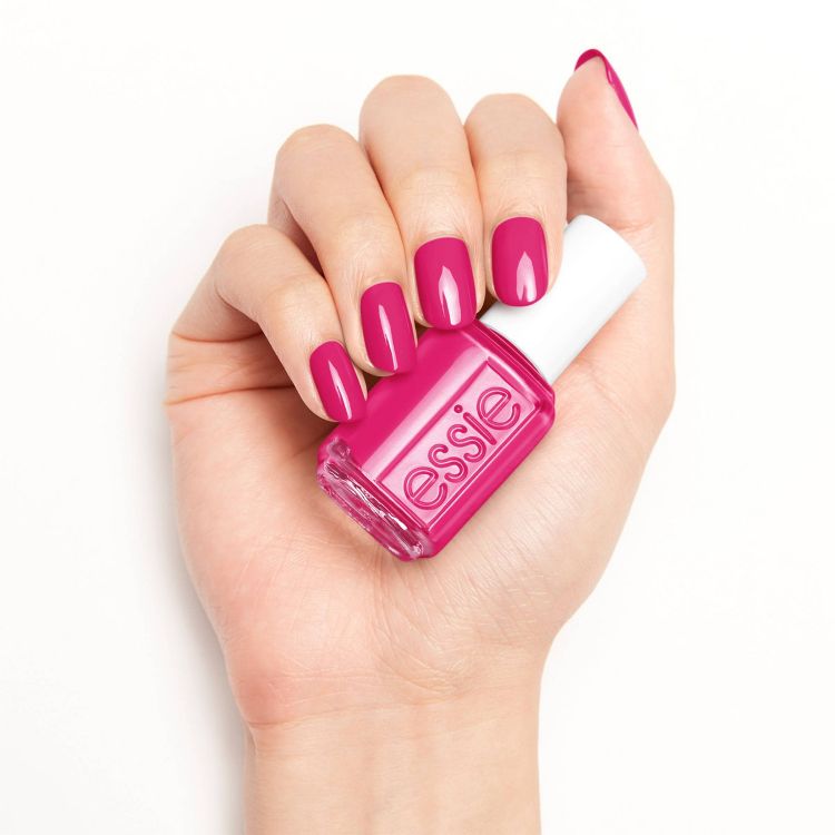 A hand holding a bottle of pink colored nail polish with matching pink colored nails, featuring the text "essie" on the bottle.