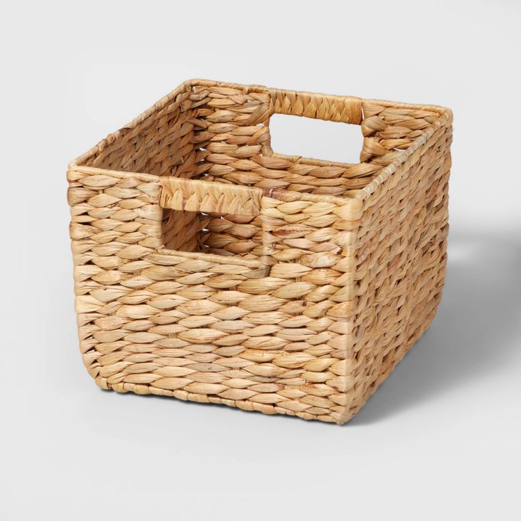 A square-shaped woven basket with integrated handles on two sides, in a natural light brown color.
