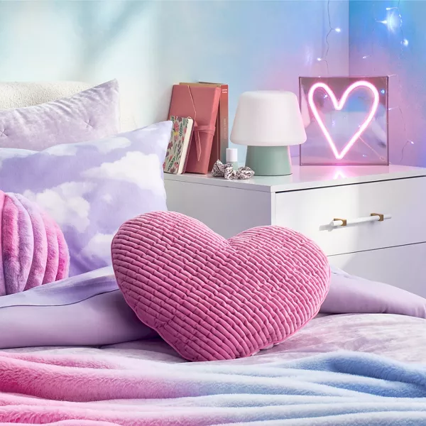 Pink & purple pastel hues bring a peaceful essence to this bedroom. Light purple pillows top the bed with cloud prints, heart shapes & soft velvet textures. Glowing lights hang on the wall & a neon pink heart light rests on the nightstand.   