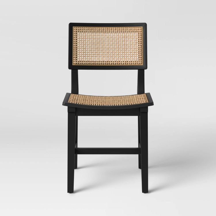 A black dining chair with a woven rattan backrest and seat.