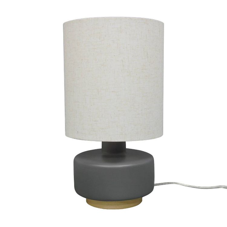 A table lamp with a white colored cylindrical shade and a gray colored base with a wooden accent.