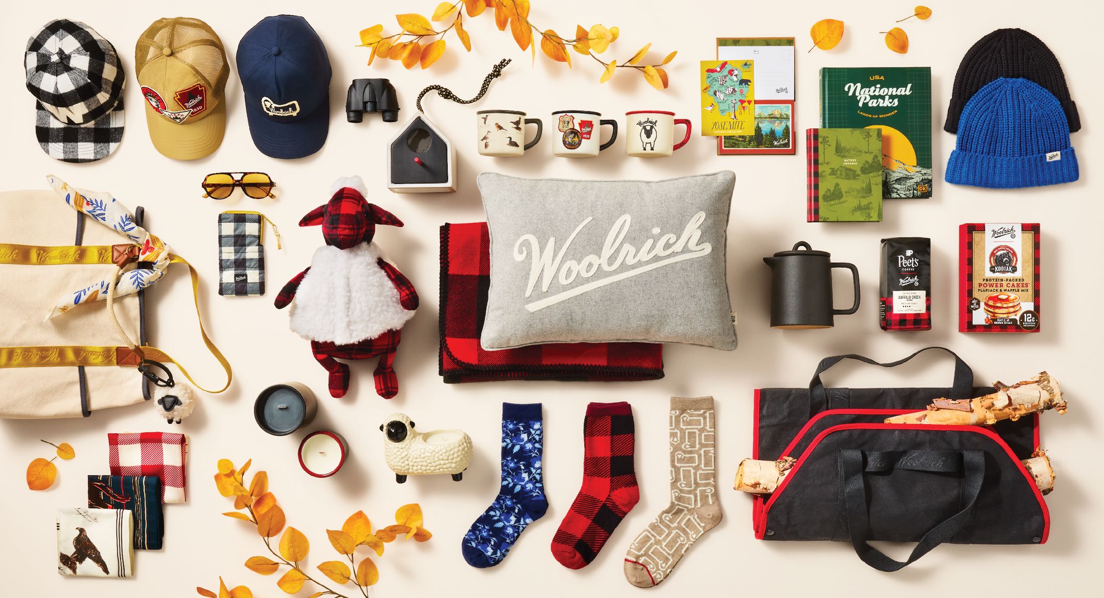 Image contains various items from the collection including graphic caps, binoculars, bird house, candles, mugs, a bird house, sunglasses, tote bag, pillows, blankets, socks, journals, beanies, pancake mix, coffee and pot, assorted bandanas and a log carrier.