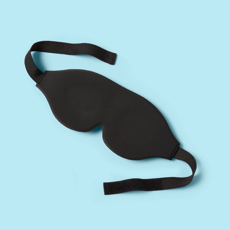 Black colored sleep mask with adjustable straps on a light blue background.