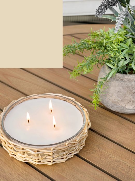 Multi wick candle sits lit on a outdoor coffee table.