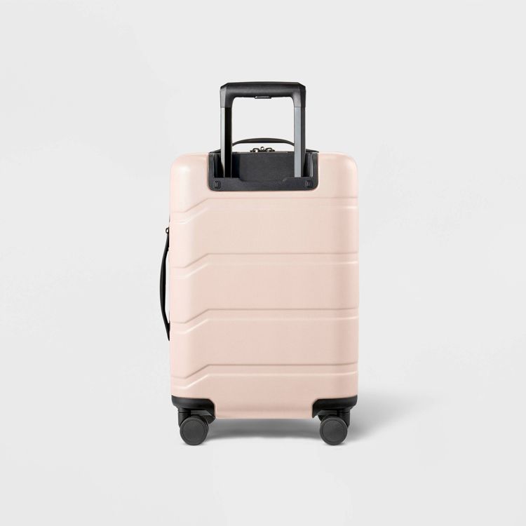 A light pink colored suitcase with a black retractable handle and four wheels.