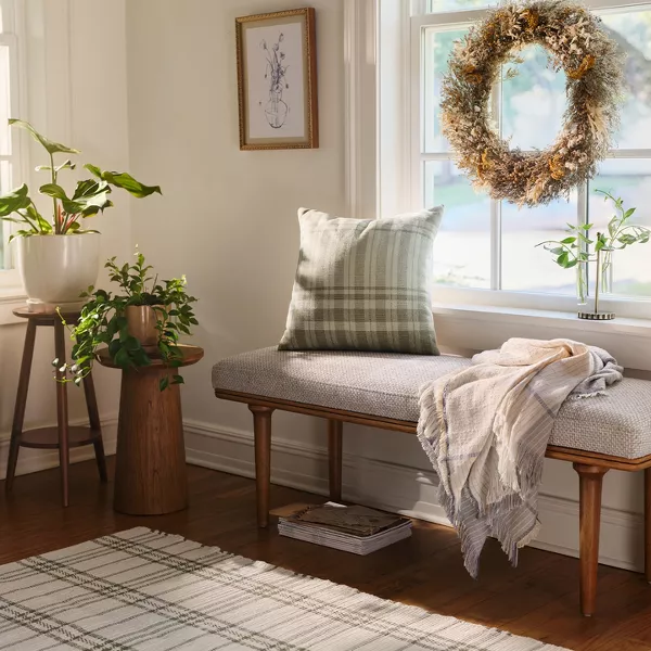 A plaid pillow and blanket on a bench in front of a sunny window.