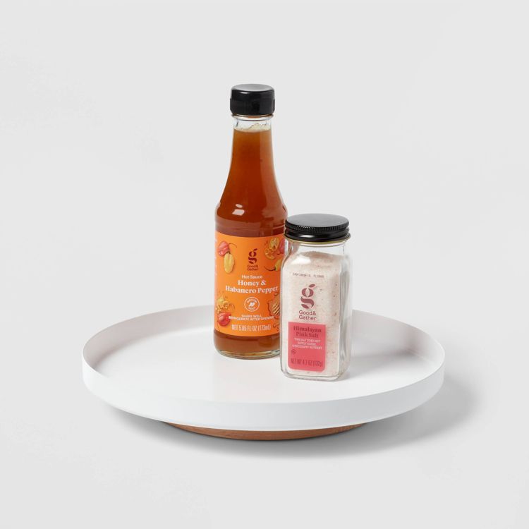 A white circular organizer holding a bottle of honey and habanero pepper hot sauce and a jar of Himalayan pink salt.