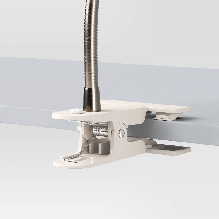 A beige colored clamp lamp attached to the edge of a light gray surface with a flexible metal neck.