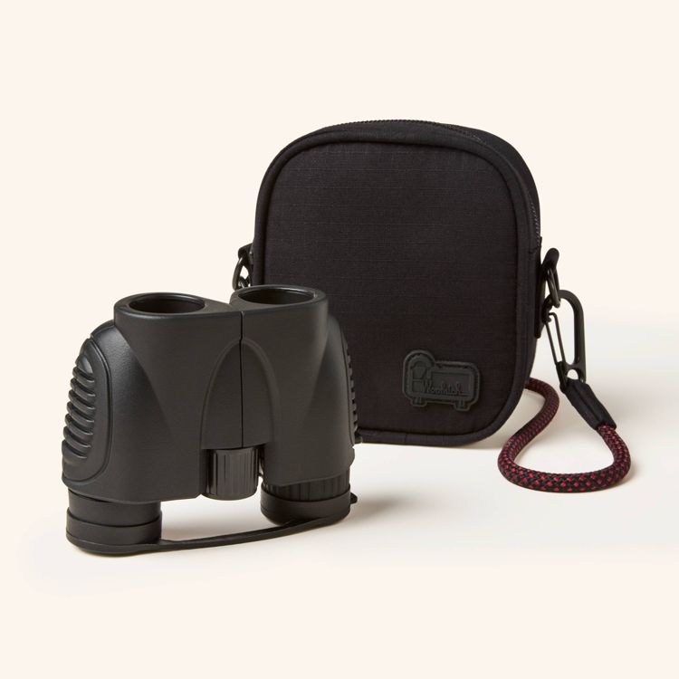 Black colored binoculars with textured grips placed next to a black carrying case with a red and black strap.