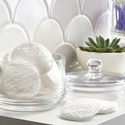 A glass container filled with white colored cotton pads next to a closed glass lid and a small green succulent plant.