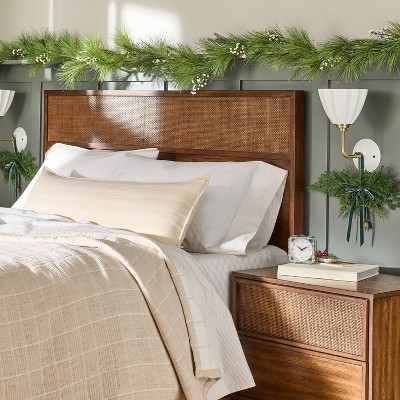 A green pine and white berry garland decorates the top of a wooden headboard in a bedroom setting.
