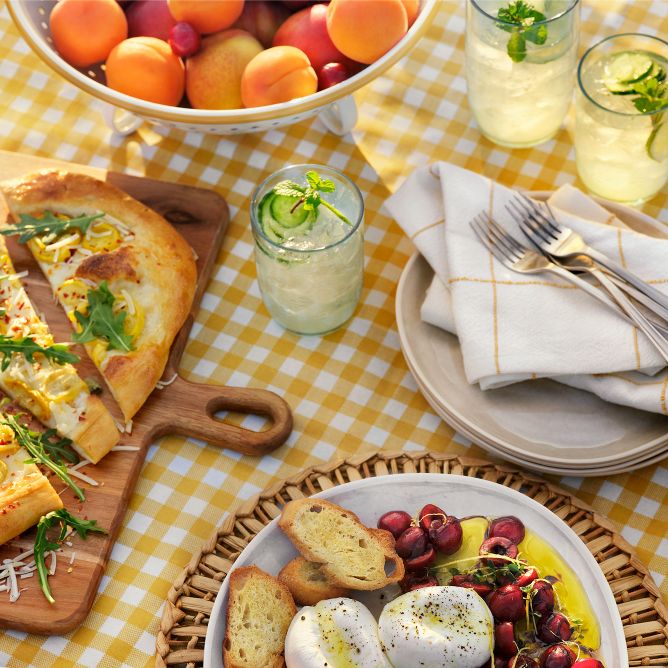 Overhead of summer table. Yellow checkered tablecloth, peaches, flatbread and lemonade. Play Video