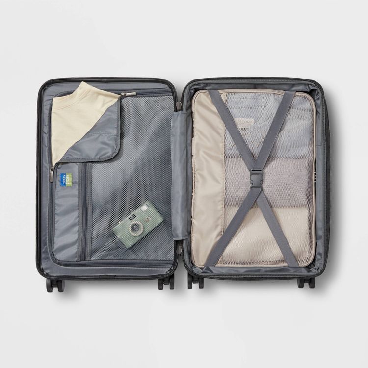 Open suitcase with a mesh pocket containing a camera and a beige colored shirt, and the other side secured with cross straps holding folded clothes.