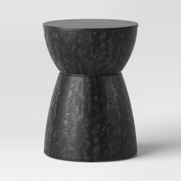 A black colored, hourglass-shaped end table with a textured surface.