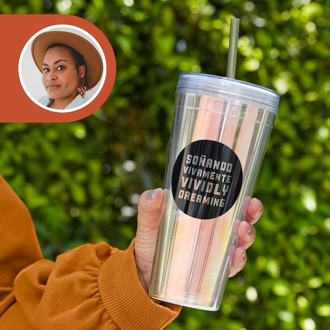 [lang=es]Una mano con una taza plateada holográfica y brillante con un círculo negro en el centro que contiene texto que dice: soñando vivamente[lang=es] [lang=en]vividly dreaming"[/lang]. 