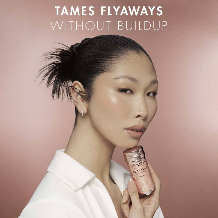 Nexxus Slick Stick Hair Wand ensures a sleek hairstyle without residue. A woman in a crisp white shirt holds the product, emphasizing controlled hair and a polished look on a soft pink backdrop.