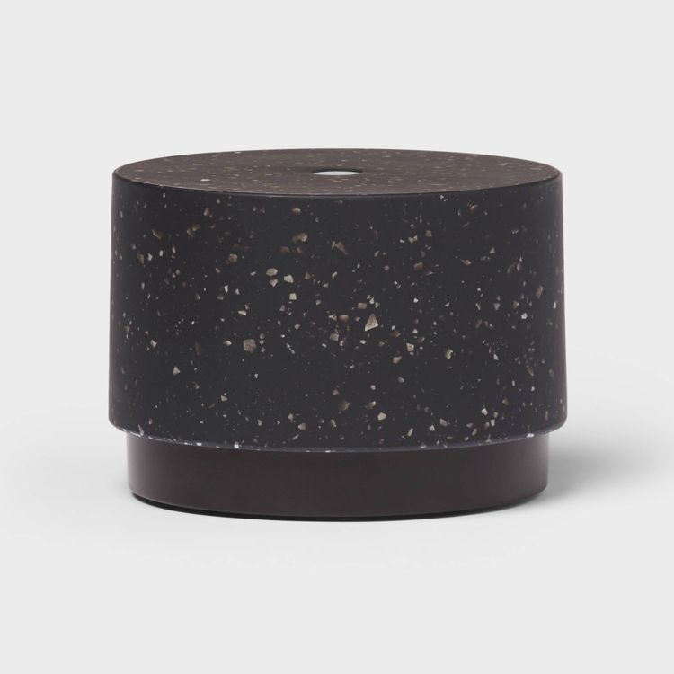 A cylindrical black colored aromatherapy diffuser with a speckled pattern on a light gray background.