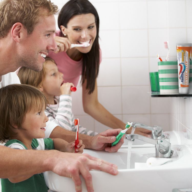 A tube of toothpaste is placed in a striped cup on a bathroom shelf next to toothbrushes.