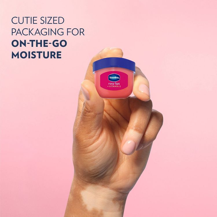 A hand holding a small container of Vaseline rosy lips with Vitamin E lip balm against a pink background, with text reading "CUTIE SIZED PACKAGING FOR ON-THE-GO MOISTURE."