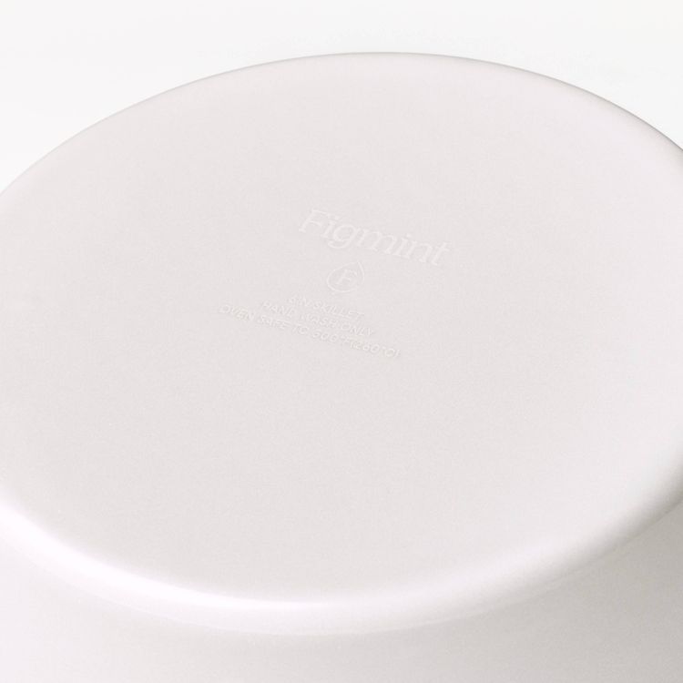 The bottom of a light-colored skillet with embossed text reading "Figmint," "8 IN SKILLET," "HAND WASH ONLY," and "OVEN SAFE TO 500°F (260°C)."