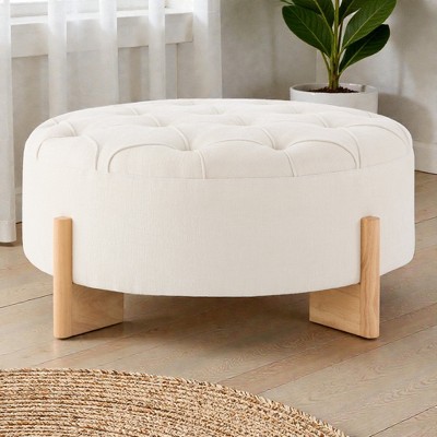 White round tufted ottoman with wooden legs on wooden floor