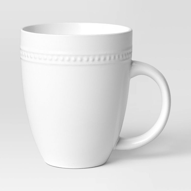 A white colored mug with a textured band near the top and a curved handle.