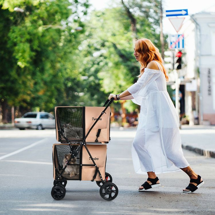 A person pushes a beige colored pet stroller with two compartments, each containing a pet, on a street.