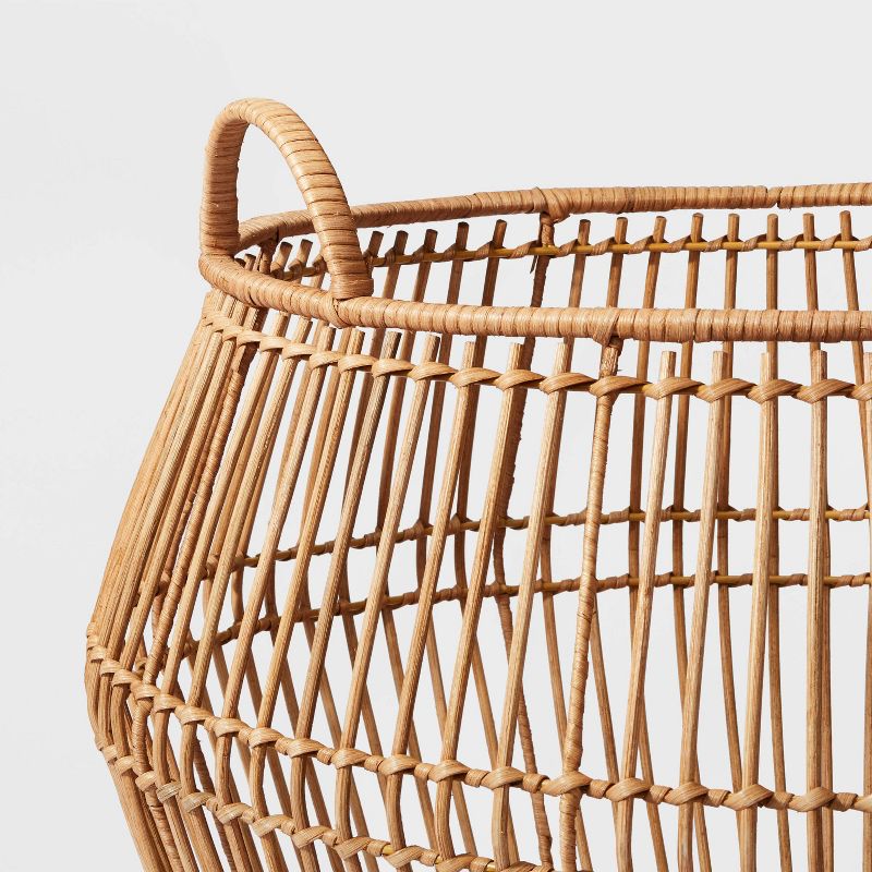 A light brown colored woven basket with a handle on a plain background.