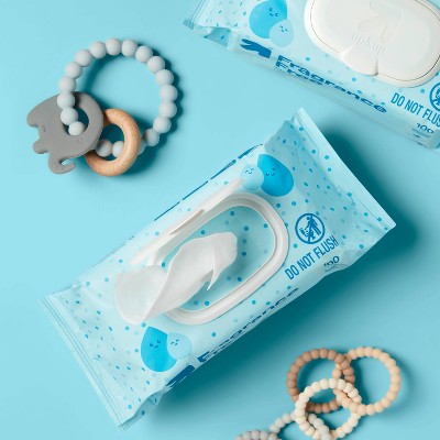 A pack of blue colored baby wipes with a "DO NOT FLUSH" label, partially opened with a wipe protruding, placed on a blue surface next to baby teething rings.