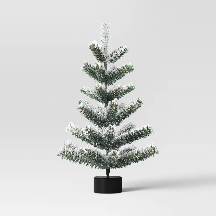A small artificial tree with green branches dusted with white, resembling snow, set in a black cylindrical base.