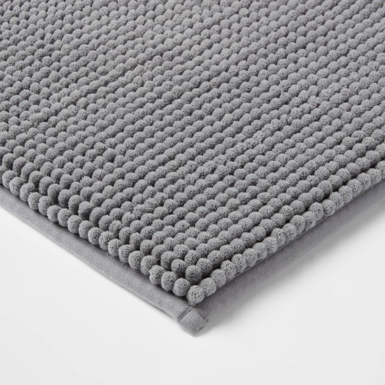 A gray colored bath mat with a textured, looped surface and a smooth border.
