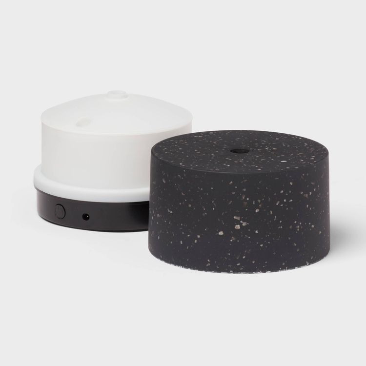 A white colored aromatherapy diffuser with a black base and a black speckled cover beside it.