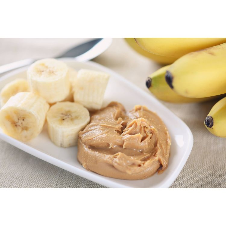 Sliced bananas and a dollop of peanut butter on a white plate with whole bananas in the background.