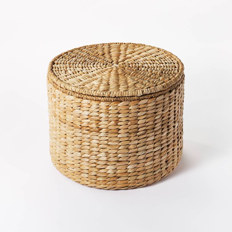 A round, woven, natural colored ottoman with a textured surface.