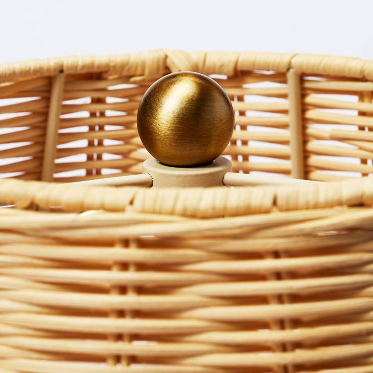 A close-up of a wicker lamp with a round gold colored knob on top.