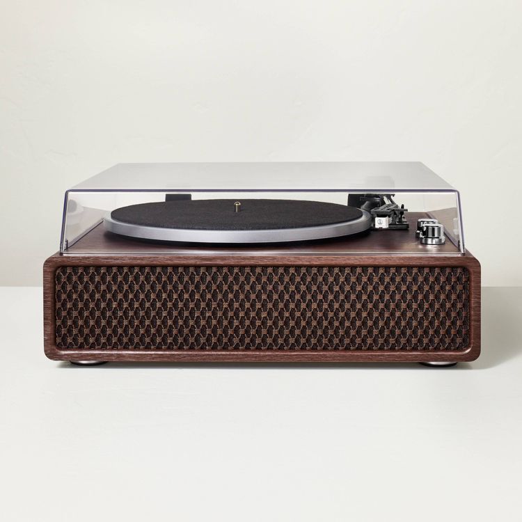 A turntable with a clear dust cover and a dark wood colored base featuring a textured front panel.