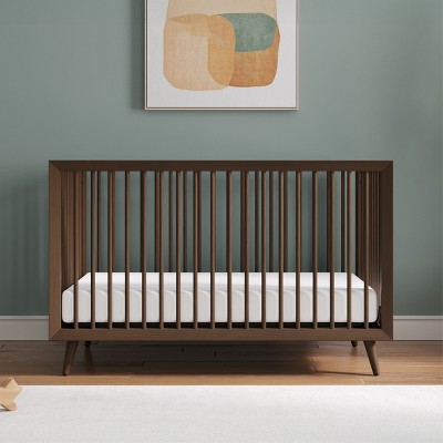 Full view of a wooden crib against a green wall with framed art above.