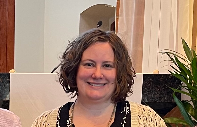 Tracy Favro, Target Cybersecurity Analyst, smiling with short brown curly hair, pictured smiling with a tan cardigan over a black v-neck shirt