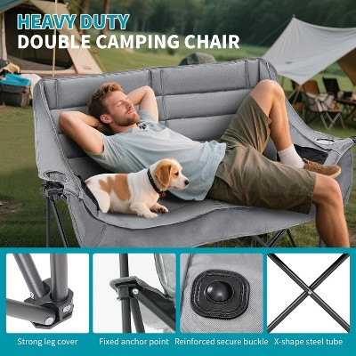 Couple relaxing on double camping chair with dog nearby